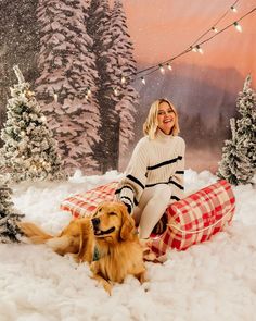 a woman sitting in the snow next to a dog and christmas tree with lights on it