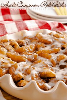 an apple cinnamon roll bake with icing on a wooden table next to plates and utensils