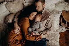 a man and woman holding a baby while laying on top of a bed next to pillows