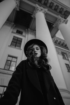 black and white photo of woman in front of building with columns on both sides, looking at camera