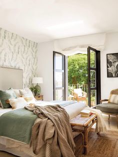 a bedroom with a large bed and two chairs in front of the window that overlooks trees