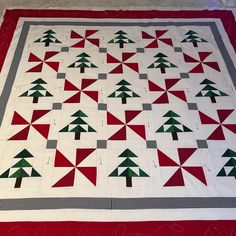 a red and white quilt with green christmas trees on the front, sitting on a floor