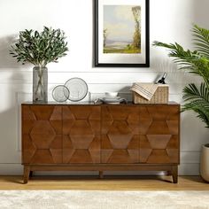 a wooden cabinet with two vases on top of it next to a potted plant