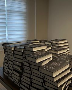 a stack of black books sitting on top of a wooden table next to a window