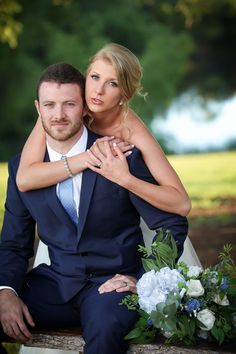 a man and woman are sitting on a bench in the park, hugging each other