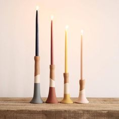 three candles are lined up in different colors and sizes on a wooden table next to each other