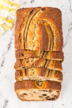 sliced loaf of banana bread sitting on top of a white counter next to a yellow flower