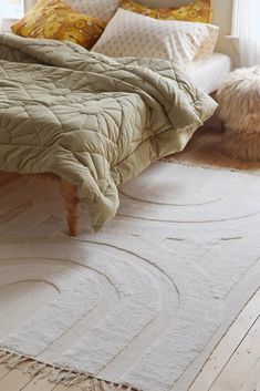 a bed sitting on top of a wooden floor next to a white rug covered in pillows