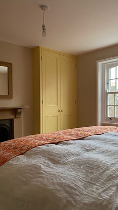 a bed with an orange comforter sitting in front of a window next to a fireplace