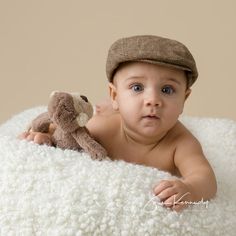 a baby in a hat is holding a stuffed animal while laying on a white blanket