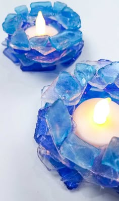 two blue glass candles are sitting next to each other on a white surface with one candle lit in the middle