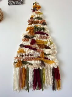 a christmas tree made out of yarn and tassels hanging on a white wall