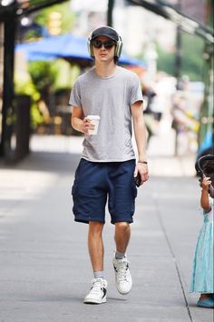 a man walking down the street while wearing headphones and holding a coffee in his hand