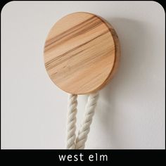 a wooden clock hanging on the side of a wall with ropes attached to it's sides