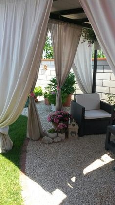 an outdoor area with white drapes and flowers on the ground, surrounded by gravel