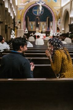 a man kneeling down next to a woman in a church while she holds her hands together