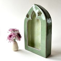 a vase with flowers in it next to a small green building shaped like a mirror