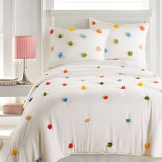 a white bed topped with lots of colorful pillows and blankets covered in pom poms