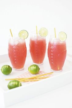 three glasses filled with watermelon and limeade sitting on a white tray next to some lemons