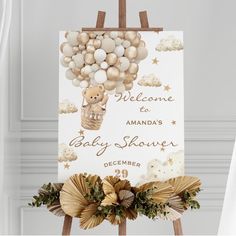 a baby shower sign hanging from a wooden easel with balloons in the shape of a teddy bear