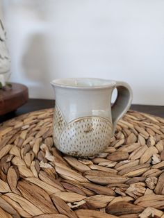 a white coffee cup sitting on top of a woven place mat next to a vase