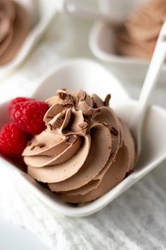 a white bowl filled with chocolate ice cream and raspberries on top of a table