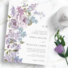 a wedding card with flowers on it next to a purple flower and green leafy plant