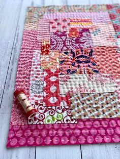 a pink patchwork placemat on a white wooden surface with a red thread laying next to it