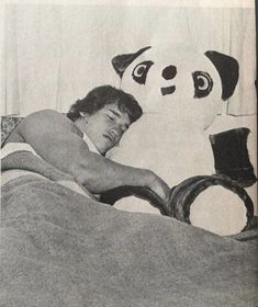 a man laying in bed next to a panda stuffed animal