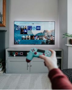 a person holding a remote in front of a flat screen tv on a entertainment center