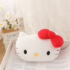 a hello kitty pillow sitting on top of an open book with a red bow in it