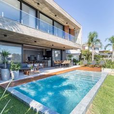 an outdoor swimming pool in front of a large house with glass doors and balconies