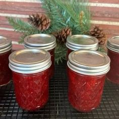 several jars filled with red liquid next to pine cones