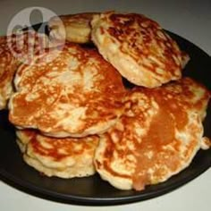 some pancakes on a black plate sitting on a white counter top with syrup pouring over them