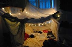 an unmade bed with lights strung from the ceiling