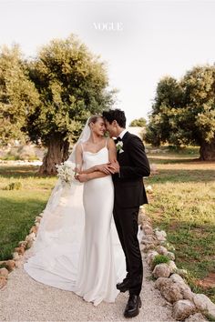 a bride and groom standing in front of a stone wall at their wedding day with the words vogle above them