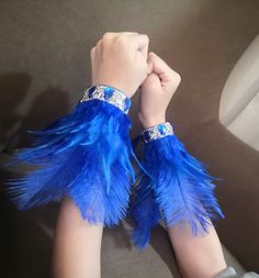 a person wearing blue feathers and bracelets on top of a couch with their hands in the air