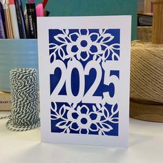 a blue and white greeting card with the number twenty five on it next to some spools of thread