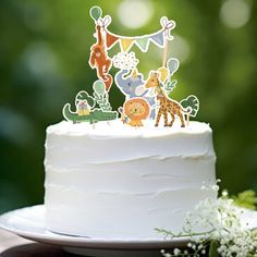 a white cake topped with a frosted animal cake topper next to greenery