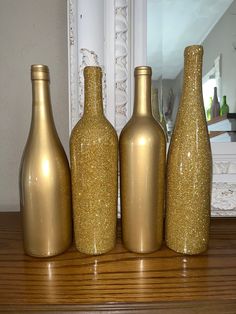 three gold colored vases sitting on top of a wooden table next to a mirror