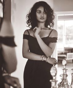 black and white photograph of a woman in a dress standing next to a glass vase