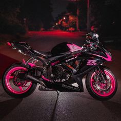 a black and pink motorcycle parked on the side of the road at night with its lights on