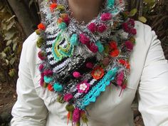 a woman wearing a multicolored crocheted scarf with flowers and feathers on it