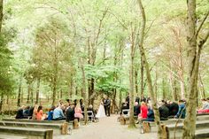 an outdoor ceremony in the woods with people sitting on benches and looking at each other