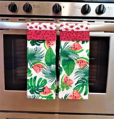 two towels hanging from the oven door with watermelon and palm leaves on them