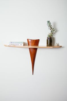 a wooden shelf with two vases and books on it next to a white wall