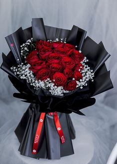 a bouquet of red roses is wrapped in black paper and sits on a white table