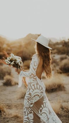 a woman in a white dress and hat is walking through the desert with her back to the camera