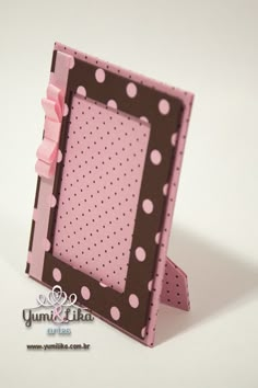 a pink and brown polka dot photo frame with ribbon on the front, sitting on a white surface