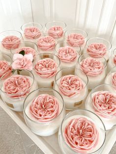 a table topped with lots of glass bowls filled with pink frosted cake and flowers